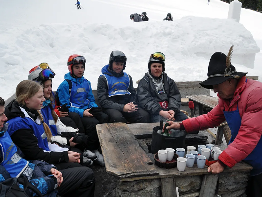 Gruppe sitzt an einem Holztisch vor einer Hütte.